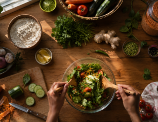 Fresh vegetables, lentils, and herbs arranged on a kitchen countertop while hands prepare a healthy homemade meal in natural morning light.