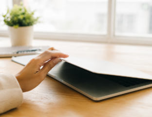 Hand closing a laptop on a wooden desk beside a notebook and plant, representing the start of a digital detox