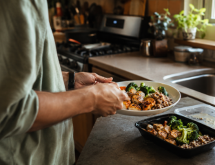 Hands portioning a home-cooked meal with chicken, broccoli, and grains into a container, an example of meal planning for weight loss