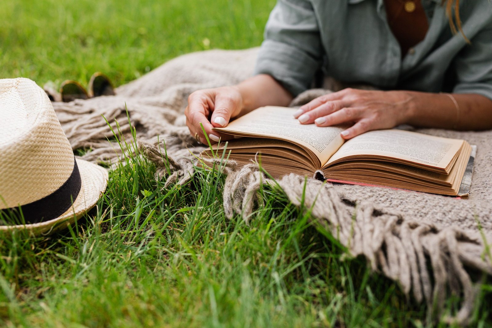 Person reading a book on a picnic blanket outdoors, no phone in sight, representing life after a digital detox